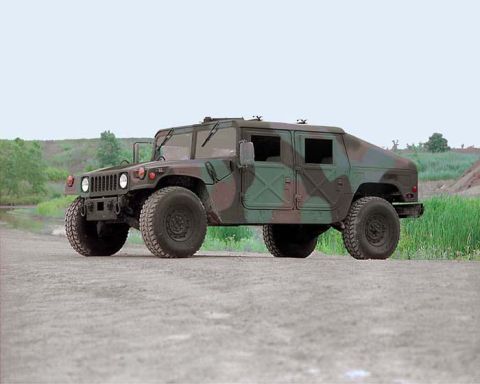 1998 Ford Crown Victoria - A military-style Humvee with camouflage paint is shown from a three-quarter front view on a dirt path.