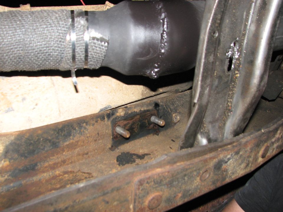 Close-up of a vehicle's exhaust pipe with metal banding, attached to a rusty frame with bolts