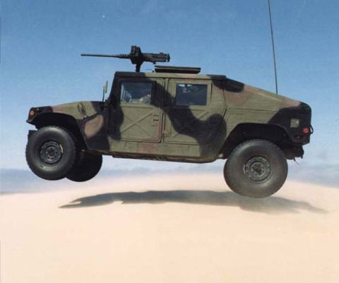 1998 Ford Crown Victoria - A military Humvee with a machine gun on top is captured mid-air over a sandy terrain.