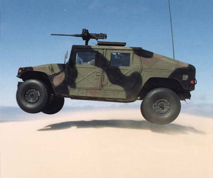 Camouflaged Humvee airborne over sand, with mounted machine gun