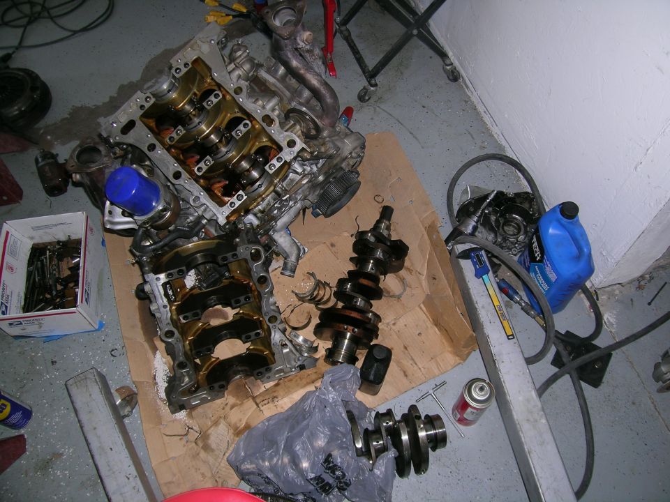 Disassembled engine block and crankshafts on a cardboard-covered floor