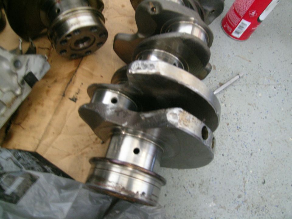 Two metal crankshafts are on a surface, one in focus, with a can of spray paint nearby