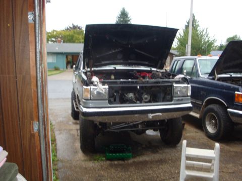 1989 Ford Bronco - Two Ford trucks are parked outside a garage, both with their hoods open, suggesting maintenance work.
