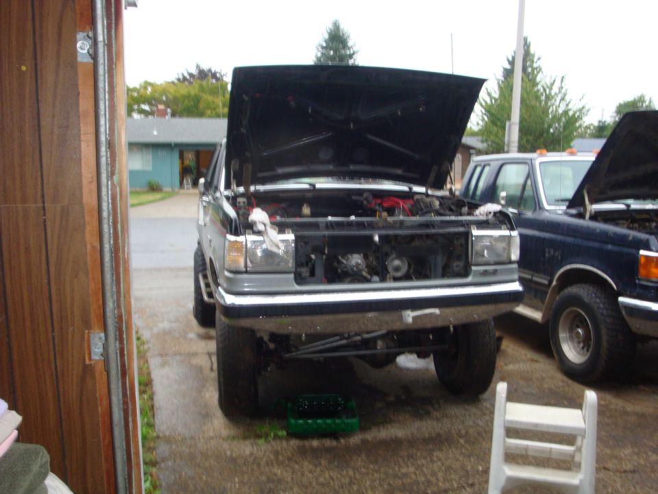 Lifted two-tone Ford truck in driveway with hood up and grille removed for engine work