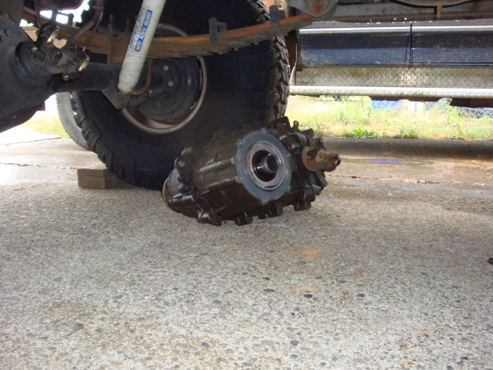 Transfer case removed from a truck resting on concrete beside the lifted rear axle