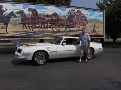 1977 Pontiac Trans Am - A white 1977 Pontiac Trans Am is parked in front of a trailer with a western mural, with a man standing beside the car.