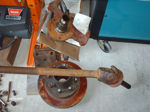 1982 Ford F-100 - A collection of rusty automotive parts, including a drive shaft and hub assembly, are laid out on a concrete floor.