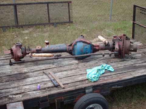 1982 Ford F-100 - A complete used solid front axle assembly laid out on the weathered wood deck of a flatbed trailer, with a blue-painted cast center section…