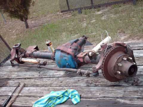 1982 Ford F-100 - A complete front drive axle assembly laid out on weathered deck boards outdoors, its housing wearing faded red paint with a blue-painted di…