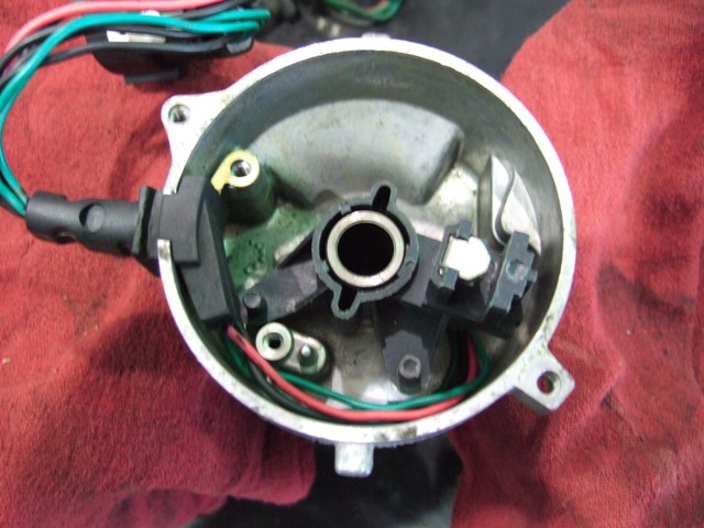 Distributor cap interior with green and red wires, black plastic components, and metal housing. Red cloth visible