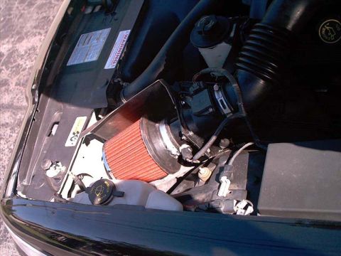 2000 Ford Crown Victoria - Cold-air intake installed in an engine bay: a red conical filter clamped to a polished aluminum intake tube with a chrome heat shield, rout…