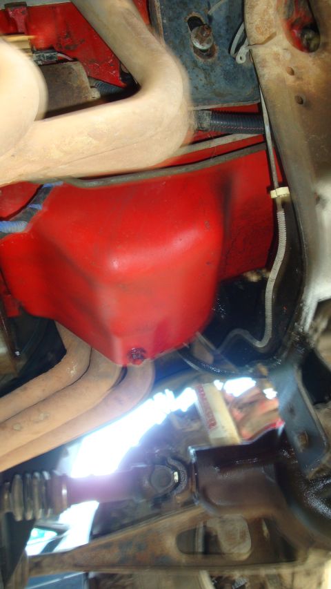 1994 Ford Bronco - Underside view of a red engine oil pan with surrounding exhaust pipes and driveshaft components.
