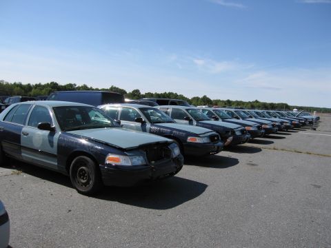 1991 Ford LTD Crown Victoria - Multiple Ford Crown Victoria police vehicles are lined up in an outdoor lot under a clear blue sky.