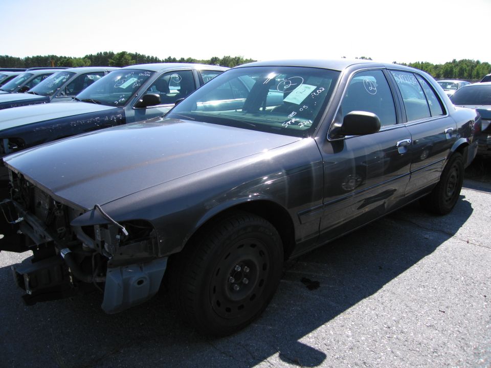 Dark sedan with missing front bumper and grille, parked in a lot with other cars