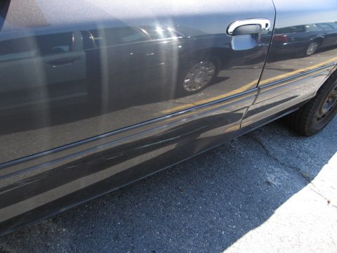 1991 Ford LTD Crown Victoria - A dark sedan's side is visible, with scratches on the lower trim and a reflection of another vehicle.