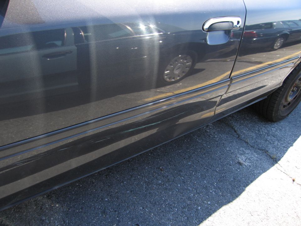 Dark sedan side door with chrome handle, showing scratches along the lower body trim