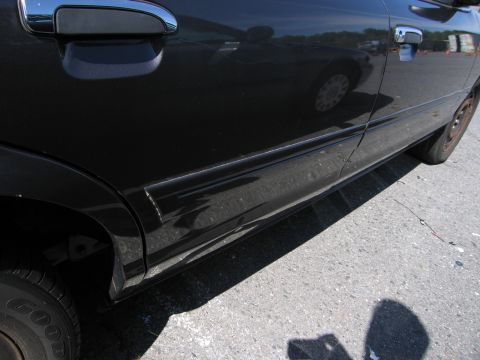 1991 Ford LTD Crown Victoria - The side of a black sedan shows damage to the lower body molding and a chrome door handle.