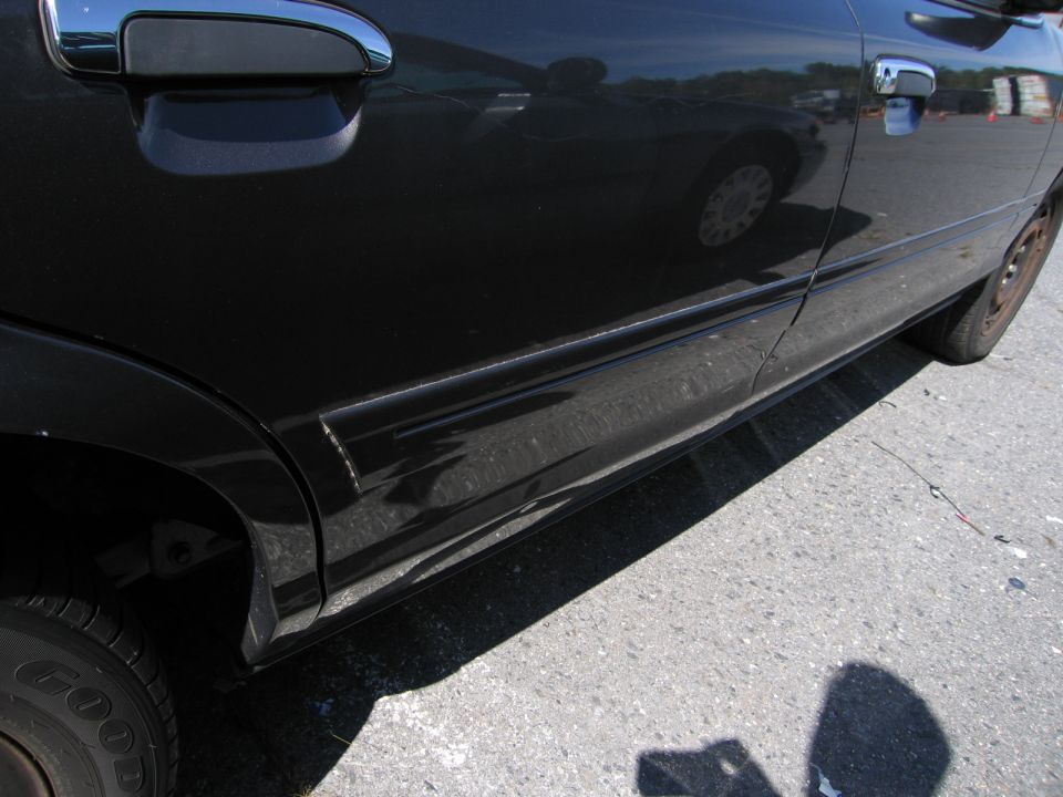 Side view of black sedan with chrome door handle and damage on lower body panel