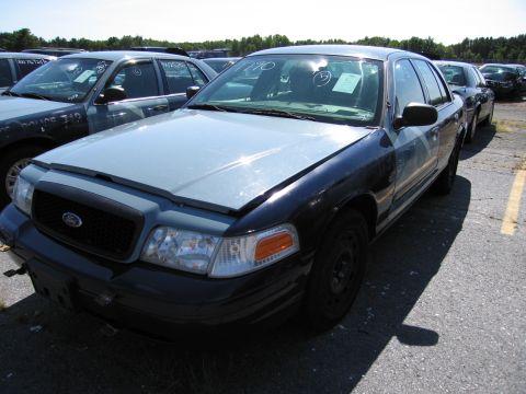1991 Ford LTD Crown Victoria - This police car, likely a Ford Crown Victoria, is parked in an outdoor lot with other vehicles visible in the background.