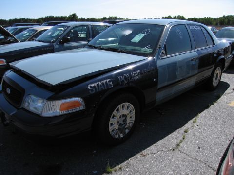 1991 Ford LTD Crown Victoria - A two-tone police car is parked in a lot with other vehicles under a clear sky.