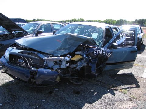 1991 Ford LTD Crown Victoria - This heavily damaged police car shows extensive front-end collision damage, with the driver's side door ajar and "STATE POLICE" lettering v…