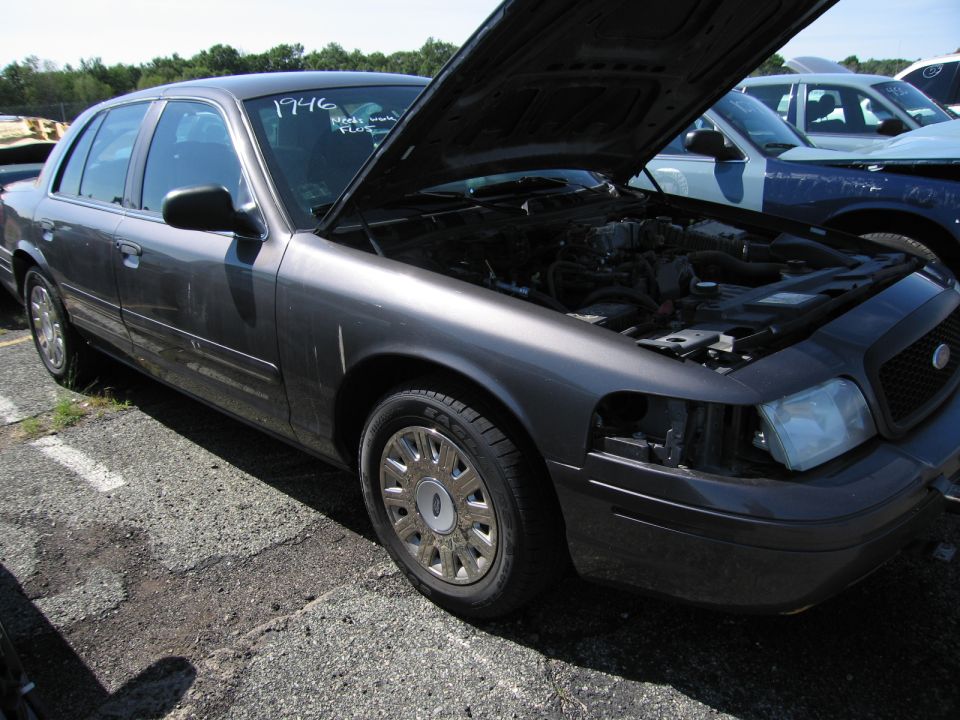 Dark gray Ford Crown Victoria with hood open, missing headlight, and "1996" written on windshield