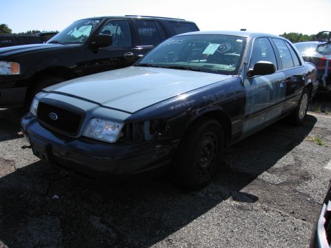 1991 Ford LTD Crown Victoria - A two-tone police car sits in a lot next to another vehicle, missing a headlight and showing signs of wear.