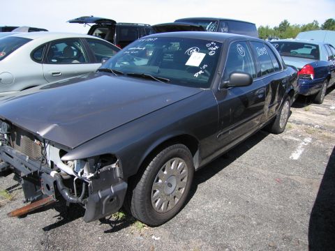 1991 Ford LTD Crown Victoria - A dark sedan with significant front-end damage sits in a vehicle lot, with other cars visible in the background.