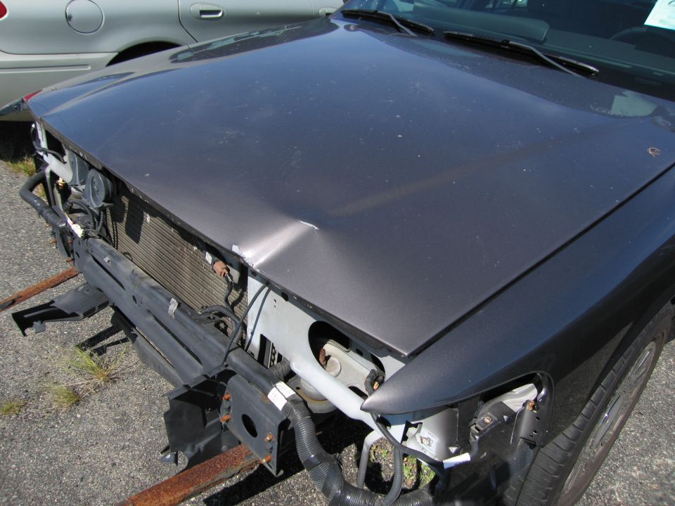 Dark gray sedan hood dented, front bumper removed, radiator exposed. Another silver car is partially visible