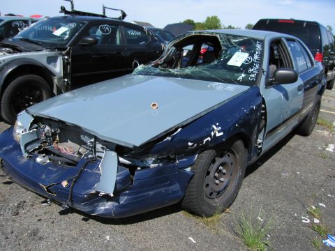 1991 Ford LTD Crown Victoria - A heavily damaged Ford Crown Victoria sits in a junkyard with other vehicles.