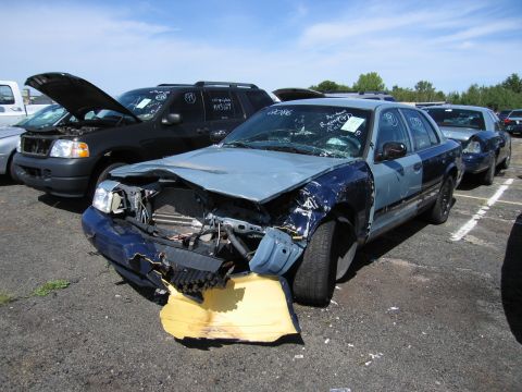 1991 Ford LTD Crown Victoria - Wrecked police car in a lot with other vehicles under a cloudy sky.
