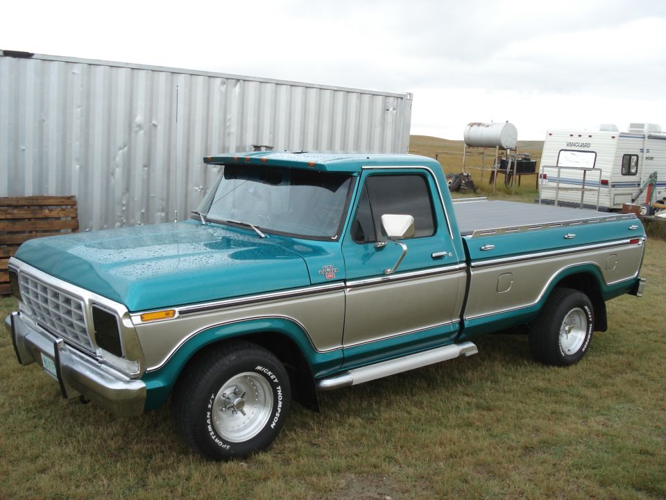 Teal and tan 1979 Ford F-150 pickup truck with a chrome grille and side steps, parked on grass