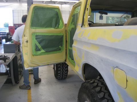 1978 Ford Bronco - A yellow 1978 Ford Bronco is being prepped for paint, with its doors open and masking tape applied.