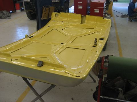 1978 Ford Bronco - The underside of a yellow car hood is displayed on a stand in a workshop setting.