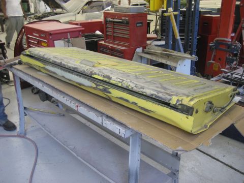 1978 Ford Bronco - A yellow tailgate, showing signs of repair and wear, is laid out on a table in a workshop environment.
