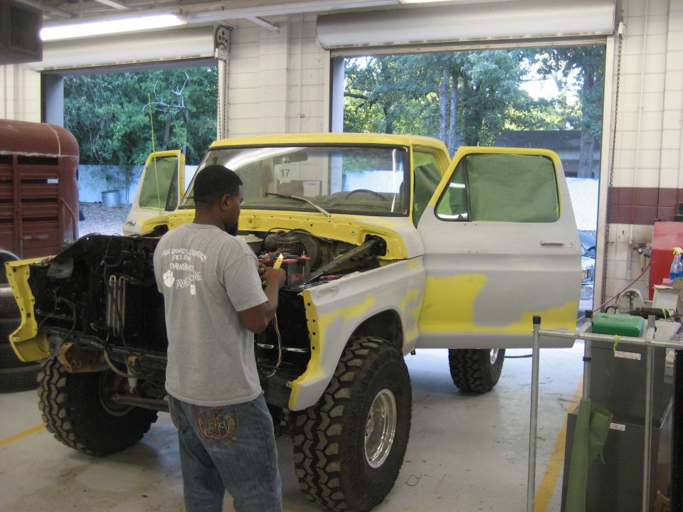 1978 Ford Bronco in yellow and grey, doors open, hood up, being worked on