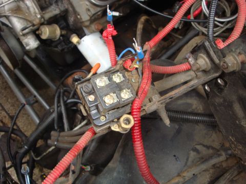 1989 Ford Bronco - Close-up view of the engine's wiring harness and fuse box, showing various electrical connections and red protective conduit.