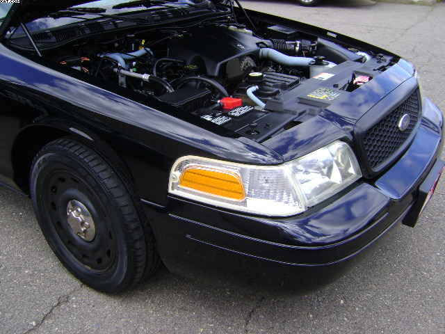 Front corner of a black 2003 Ford Crown Victoria with the hood open, showing the engine bay. The grille and headlight are visible