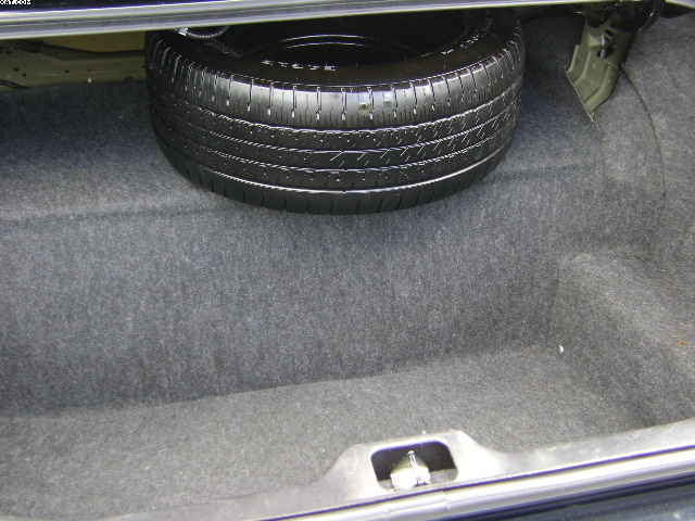 Spare tire in trunk of a car, carpeted interior, metal latch visible