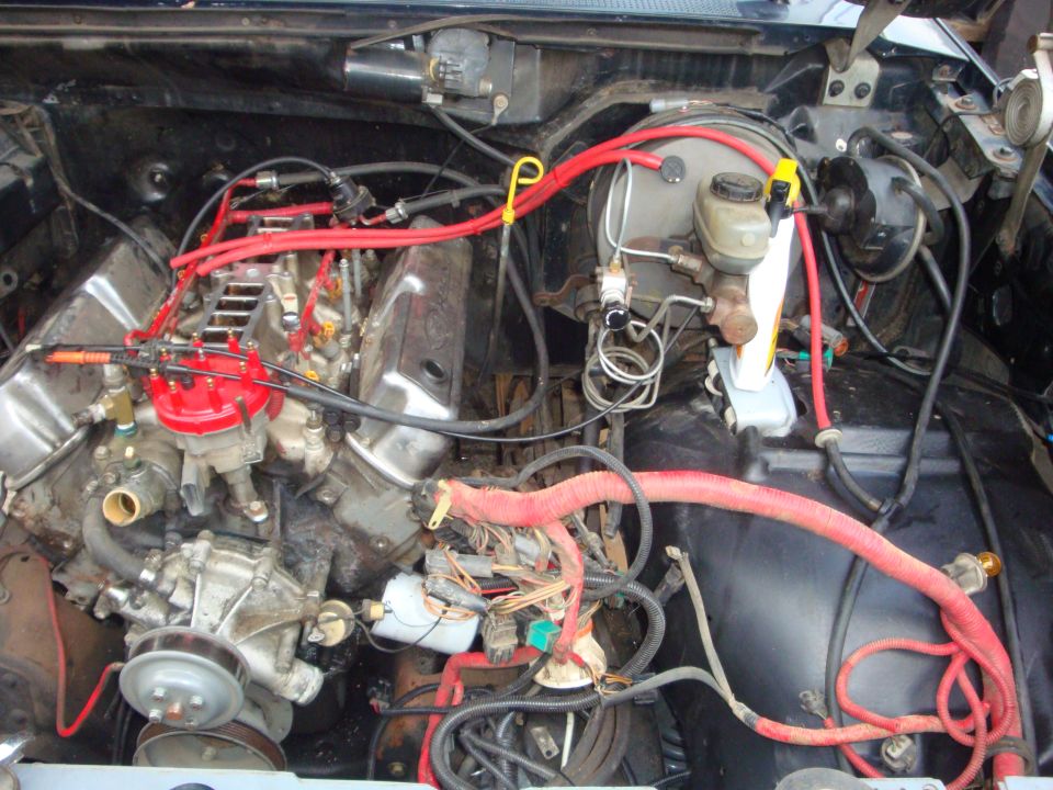 V8 engine bay mid-swap with red distributor cap, plug wires and loose harness