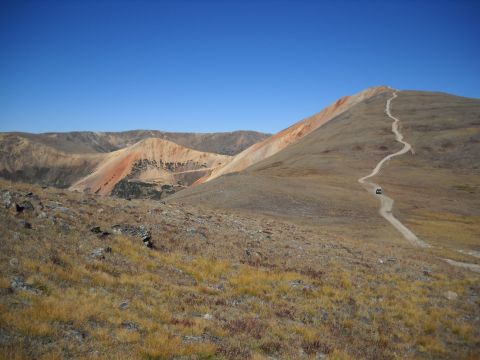 1986 Ford Bronco II - A lone black SUV navigates a winding dirt road up a barren mountain under a clear blue sky.