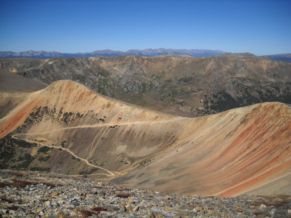 Mountain landscape with a winding dirt road and distant mountains under a clear blue sky