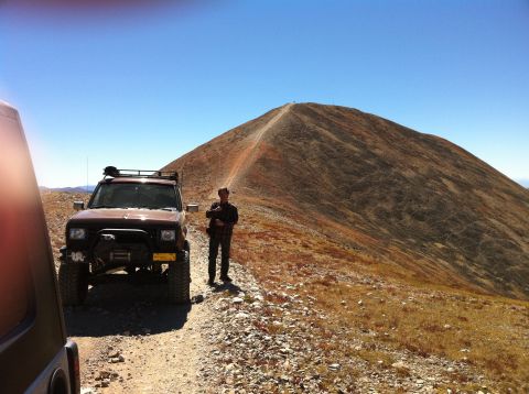 1986 Ford Bronco II - A 1986 Ford Bronco II is parked on a mountain trail, with a person standing beside it and another vehicle partially visible in the foregrou…