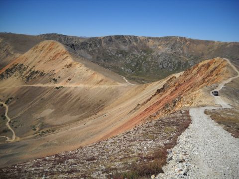 1986 Ford Bronco II - A vehicle travels a narrow dirt road on a steep mountain pass with colorful rock formations.