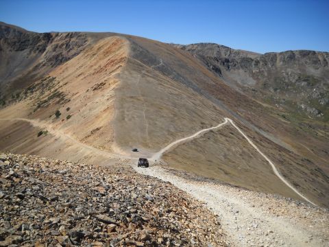 1986 Ford Bronco II - Off-road vehicles navigate a narrow, dusty trail high in the mountains.
