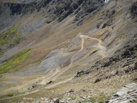 1986 Ford Bronco II - A winding dirt road ascends a steep, rocky mountainside. The area has sparse vegetation and appears to be at a high elevation.