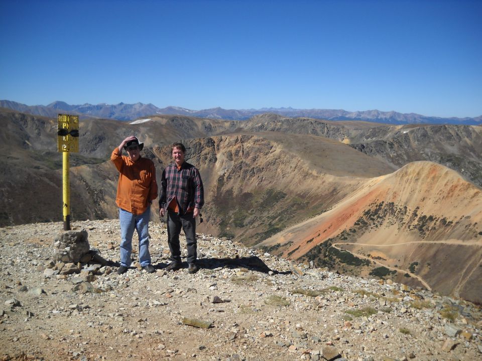 Two men stand on a rocky mountain peak under a clear blue sky