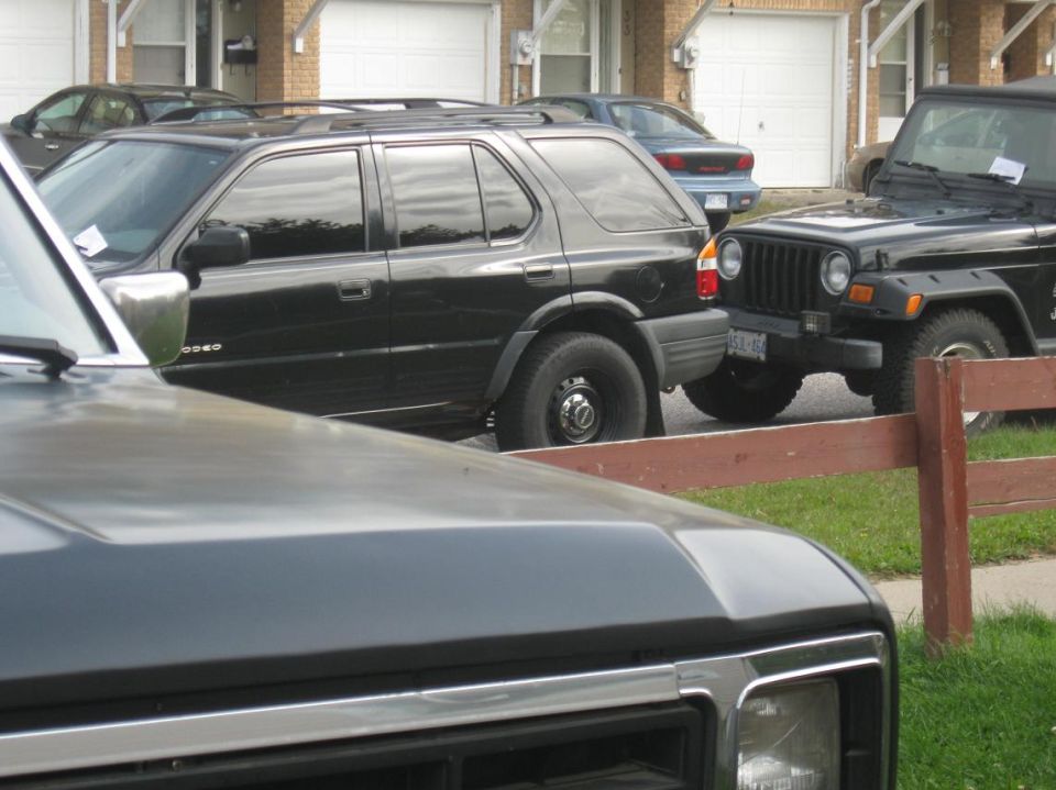 Black SUV parked next to a black Jeep Wrangler in front of garages