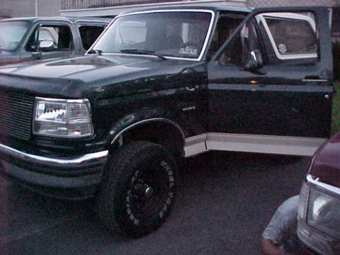 1993 Ford Bronco - This dark green 1993 Ford Bronco is parked next to another vehicle with its driver's door ajar.