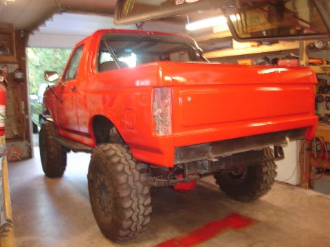 1989 Ford Bronco - Orange 1989 Ford Bronco with off-road tires sits in a garage, possibly undergoing restoration.